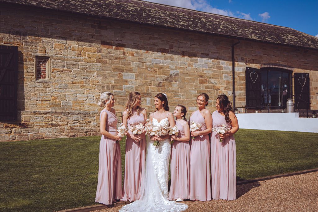 A bride and her bridesmaids standing outside of their East Sussex wedding venue Hendall Manor Barn with their romantic blush and white bouquets