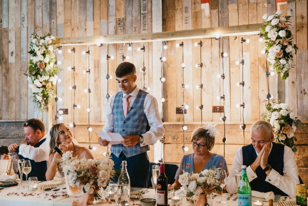 Wedding Breakfast celebrations at East Sussex wedding venue Montague Farm as the couple sit in front of a huge wedding flower archway