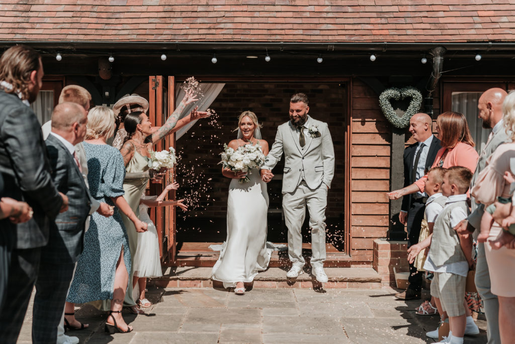 A couple walking out of their wedding ceremony at Long Furlong Barn West Sussex with the Bride holding her lush white bridal bouquet